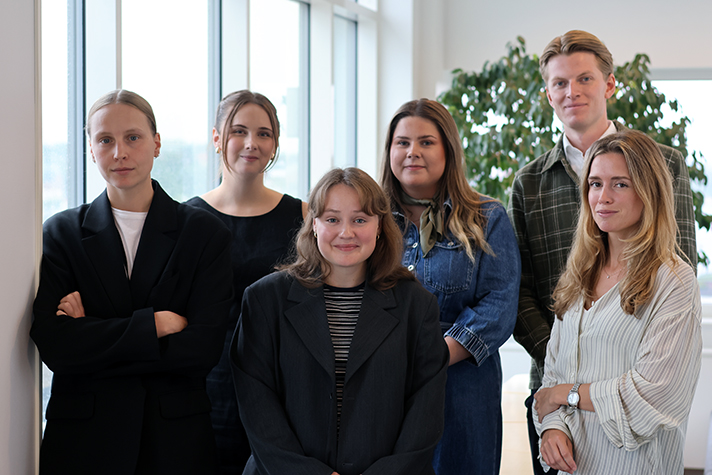 Fem kvinnor och en man står framför ett fönster.