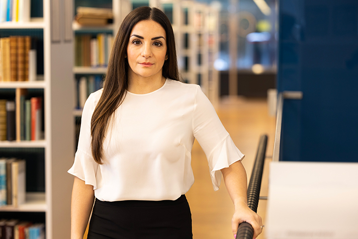 Porträtt på Parisa Liljestrand som står framför en rad bokhyllor