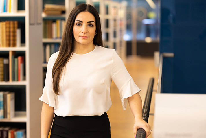 Porträtt på Parisa Liljestrand som står framför en rad bokhyllor
