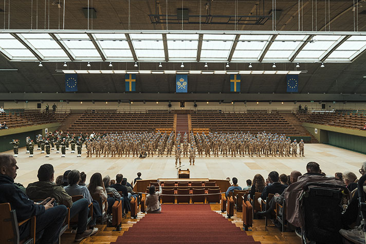 Svenska FN-soldater i ökenkamouflage står uppställda längs ena långsidan av centercourt i Kungliga Tennishallen. 