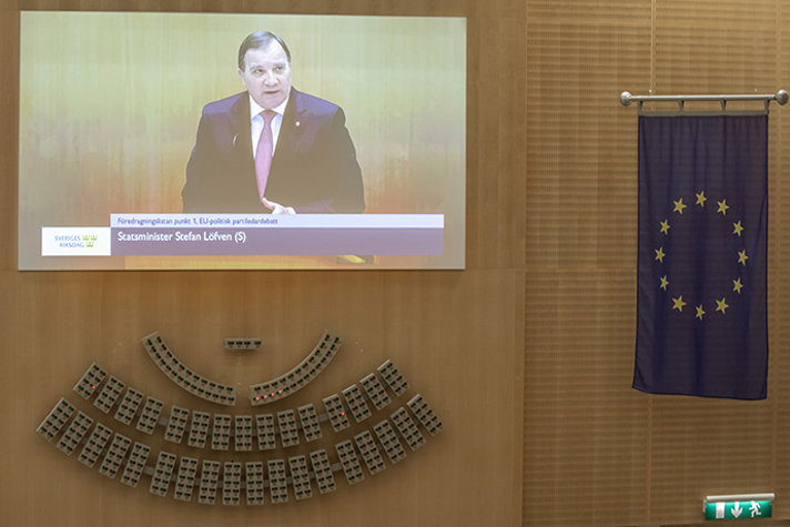 Stefan Löfven visas på en storskärm i riksdagen.