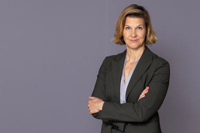 Jämställdhetsminister Nina Larsson står framför en grå vägg och tittar in i kameran.