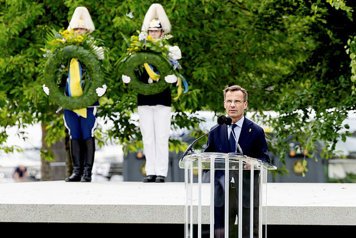 Statsminister Ulf Kristersson i en talarstol. Två soldater i gammaldags uniformer står bakom ministern och håller var sin lagerkrans.