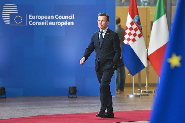 Ulf Kristersson går på en röd matta på väg in till möte i Europeiska rådet. I förgrunden EU:s flagga.