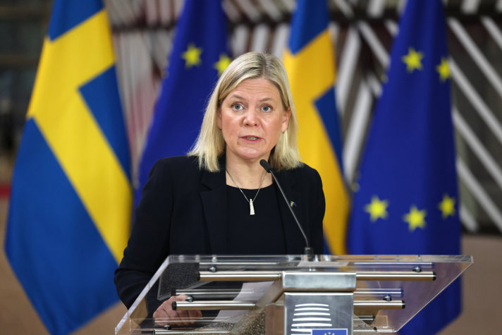 Statsminister Magdalena Andersson står i en talarstol och  talar. Framför svenska flaggor och EU-flaggan.