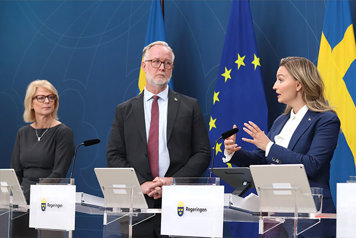 Elisabeth Svantesson, Johan Pehrson och Ebba Busch står vid varsin talarstol i regeringens pressrum. I bakgrunden svenska flaggor och EU-flaggan.
