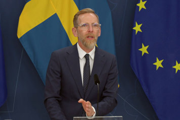 Statsrådet är avbildad i halvfigur och står vid en talarpulpet. I fonden syns svenska fanan.