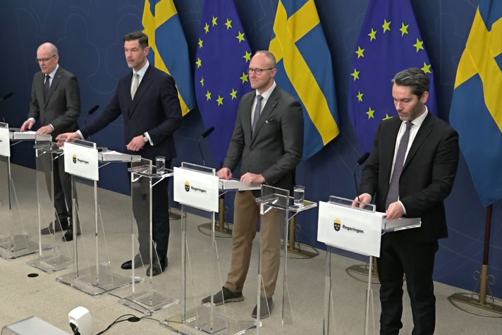 De fyra medverkande fotograferade i helfigur snett framifrån vid vart sin talarstol.