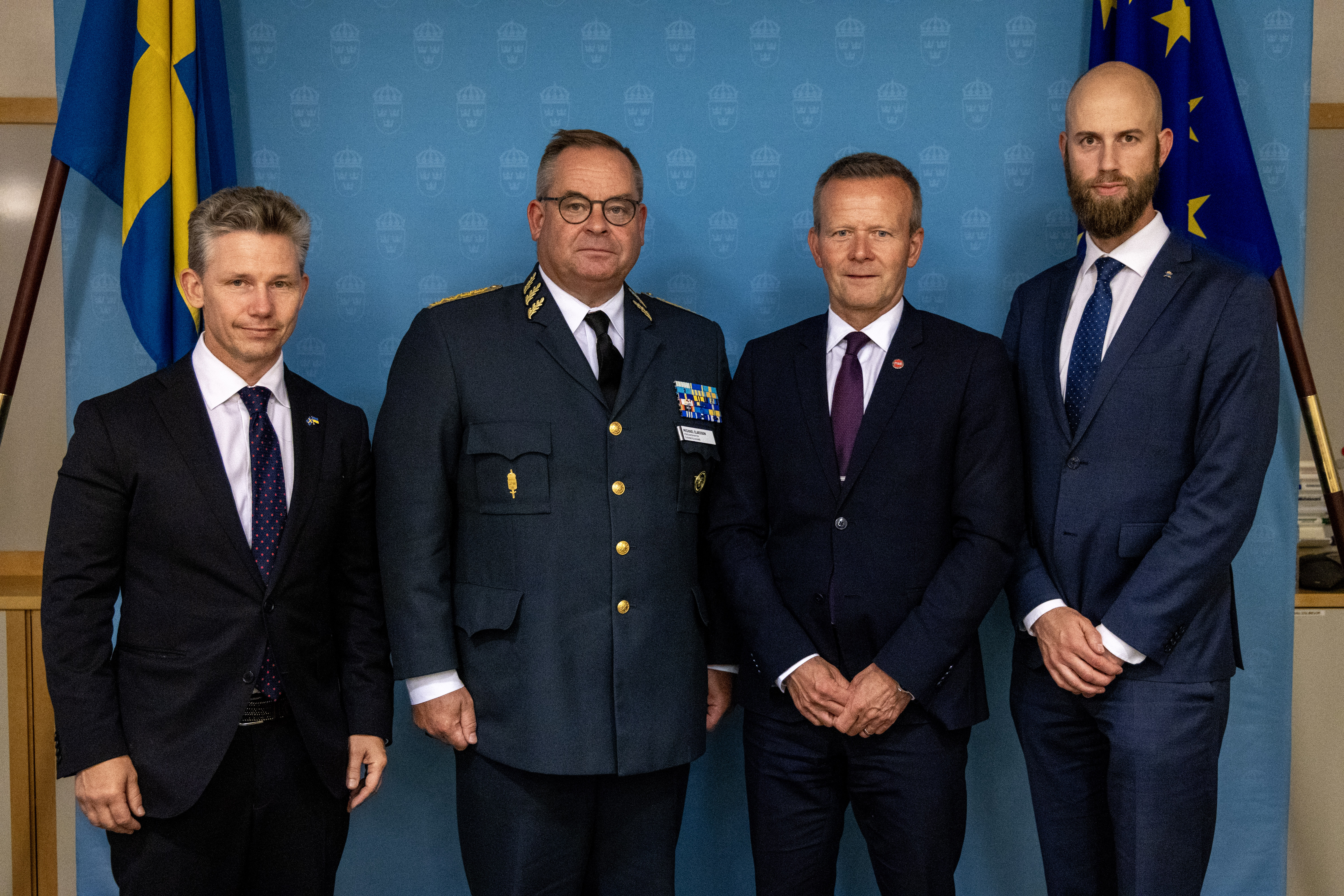 Försvarsminister Pål Jonson, överbefälhavare Michael Claesson från Försvarsmakten, Mikael Frisell, generaldirektör för MSB, och minister för civilt försvar Carl-Oskar Bohlin stående framför en blå vägg med flaggor.