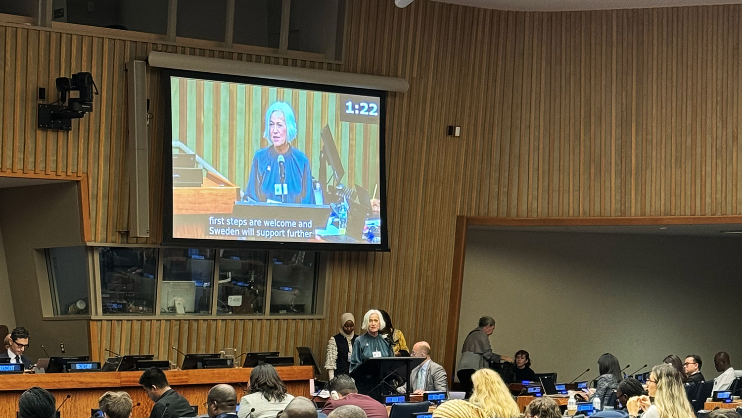 Acko Ankarberg Johansson håller ett tal bakom en talarstol. Hennes ansikte syns på en storbildsskärm bakom henne.