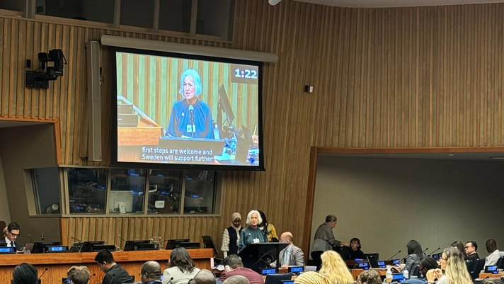 Acko Ankarberg Johansson håller ett tal bakom en talarstol. Hennes ansikte syns på en storbildsskärm bakom henne.