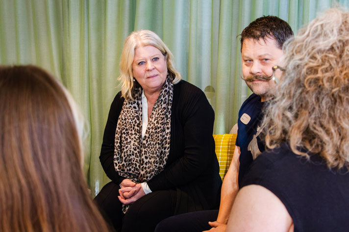 Inomhusbild. Waltersson Grönvall sitter vänd mot kameran, med en person bredvid sig och två framför sig, i ett fokuserat samtal. Bakgrunden är täckt av hängande gardiner.