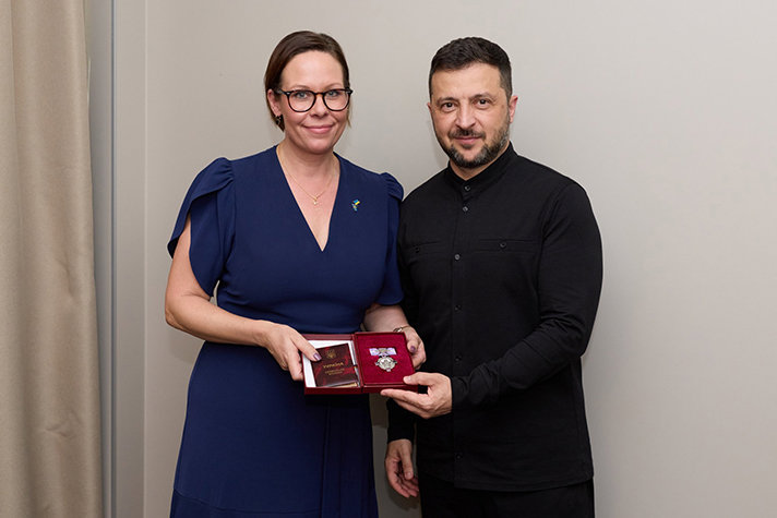 Inomhusbild på Stenergard och Zelenskyj i halvfigur mot grå bakgrund. De står bredvid varandra vända mot kameran. Stenergard håller fram ett etui med en medalj i, och Zelenskyj håller sin vänsterhand under nedre delen av etuiet.