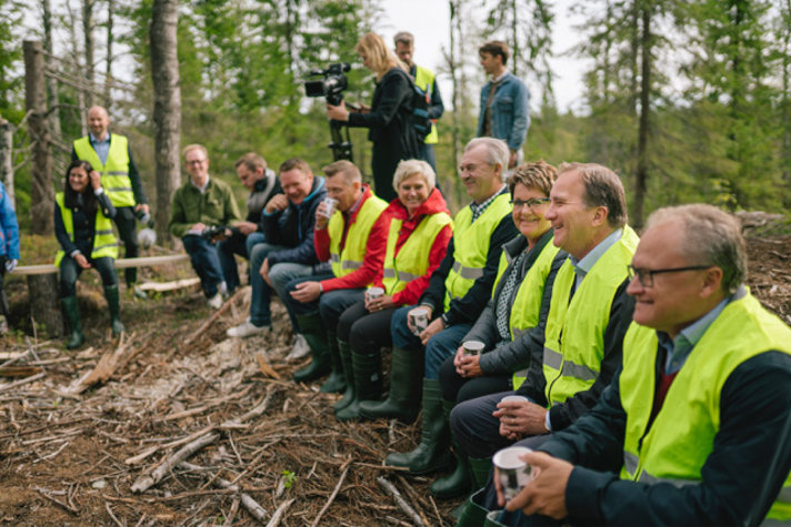 Stefan Löfven och Sven-Erik Bucht sitter i en skogsglänta och samtalar med en grupp människor.