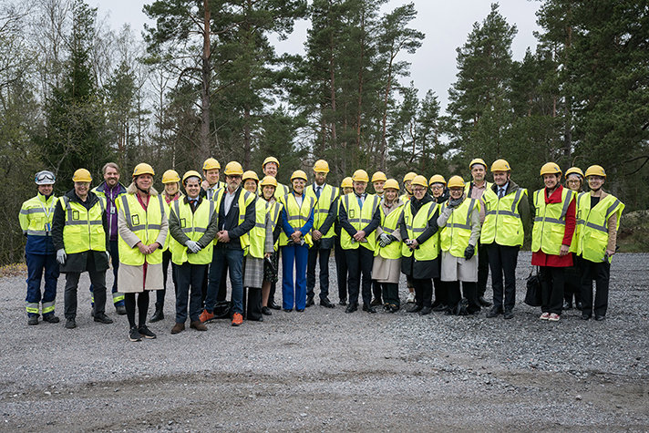 Flera personer står på rad utomhus iklädda gula hjälmar och reflexvästar.
