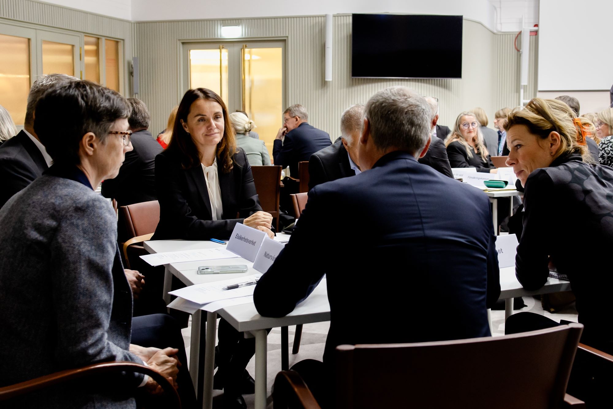 Flera personer sitter runt bord och diskuterar.