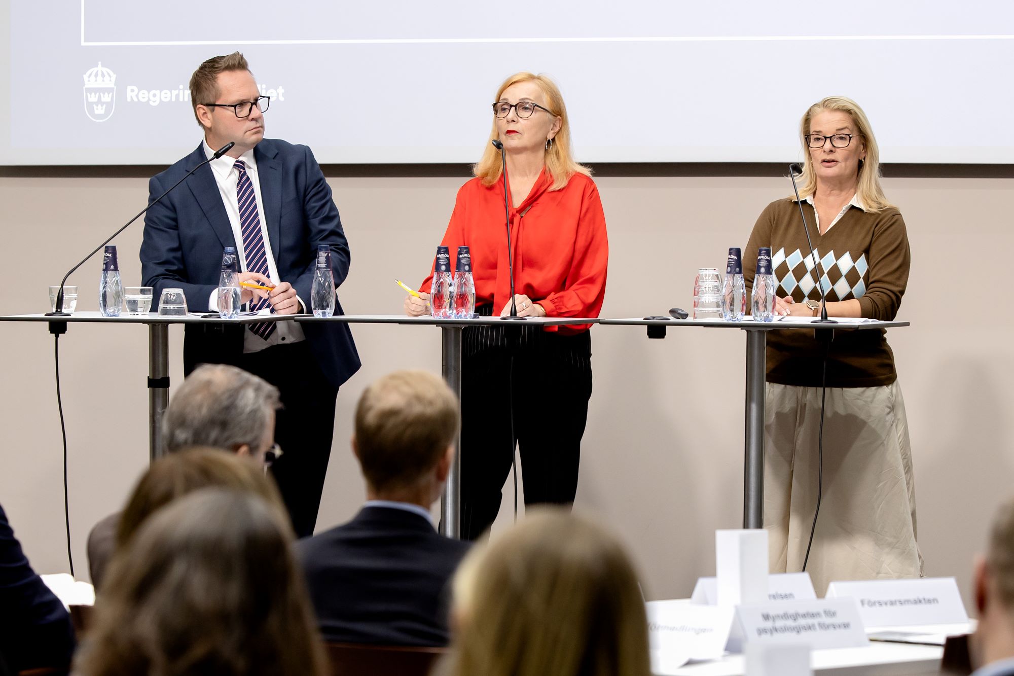 Tre personer står på en scen och pratar.