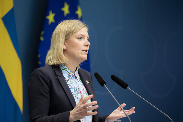 Finansminister Magdalena Andersson på en pressträff framför en svensk flagga och en EU-flagga.