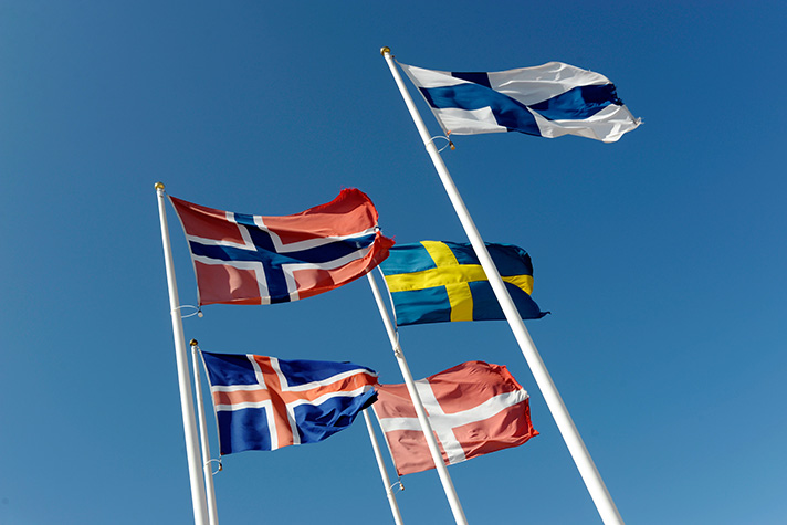 Nordens flaggor fladdrar i vinden  på flaggstänger sett strax nedanfrån