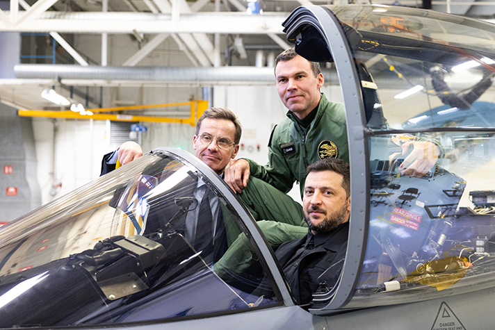 Ulf Kristersson, Volodymyr Zelenskyj och Marcus Wandt sitter i ett JAS Gripen som står i en hangar.