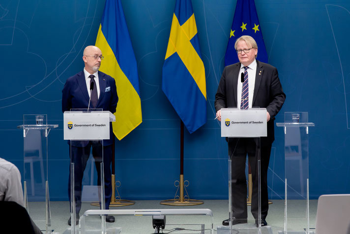 Oleksii Reznikov och Peter Hultqvist i kostym framför varsin talarstol inomhus.