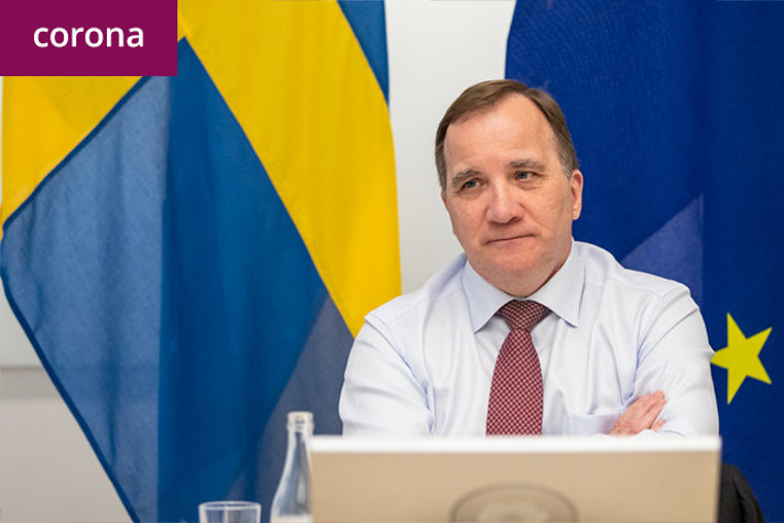 Statsminister Stefan Löfven sitter framför den svenska flaggan och EU-flaggan.