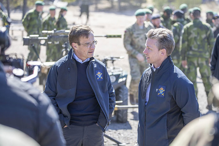 Statsminister Ulf Kristersson står och pratar med försvarsminister Pål Jonson. I bakgrunden syns amfibiesoldater och soldater ur Royal Marines