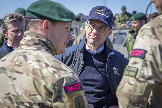 Ulf Kristersson iklädd en marinblå keps med texten HMS Albion står och pratar med befäl ur Royal Marines