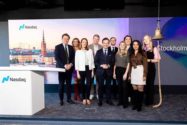 Ulf Kristersson och Roberta Metsola står med åtta andra på en gruppbild. Till vänster om gruppen syns aktiebörsen Nasdaqs logotyp, och till höger hänger börsens klocka i ett rep.
