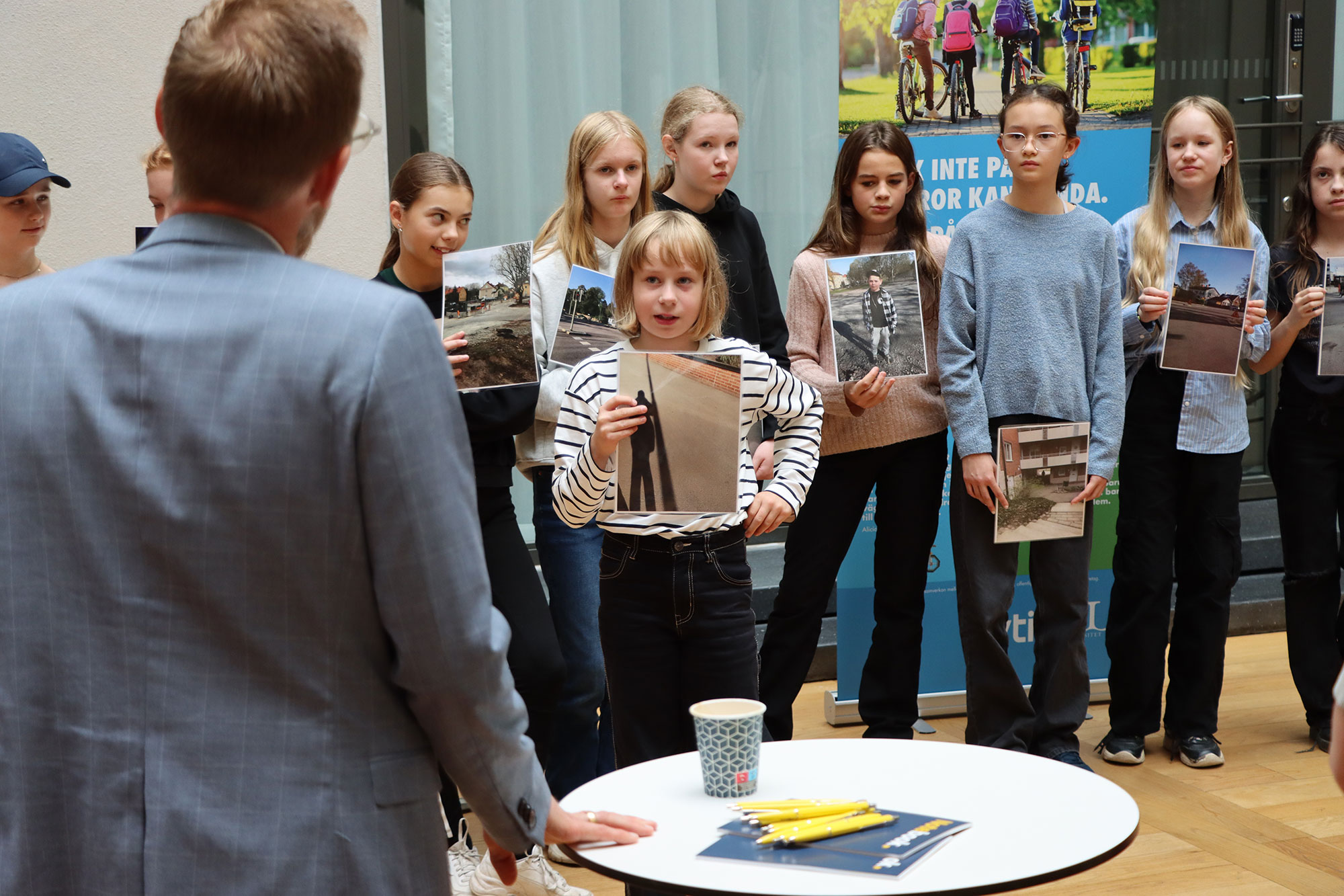 En flicka håller upp ett foto på en gata. I förgrunden står en man i grå kavaj.