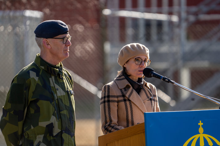 Jessika stående utomhus i kappa och basker vid en talarstol.
