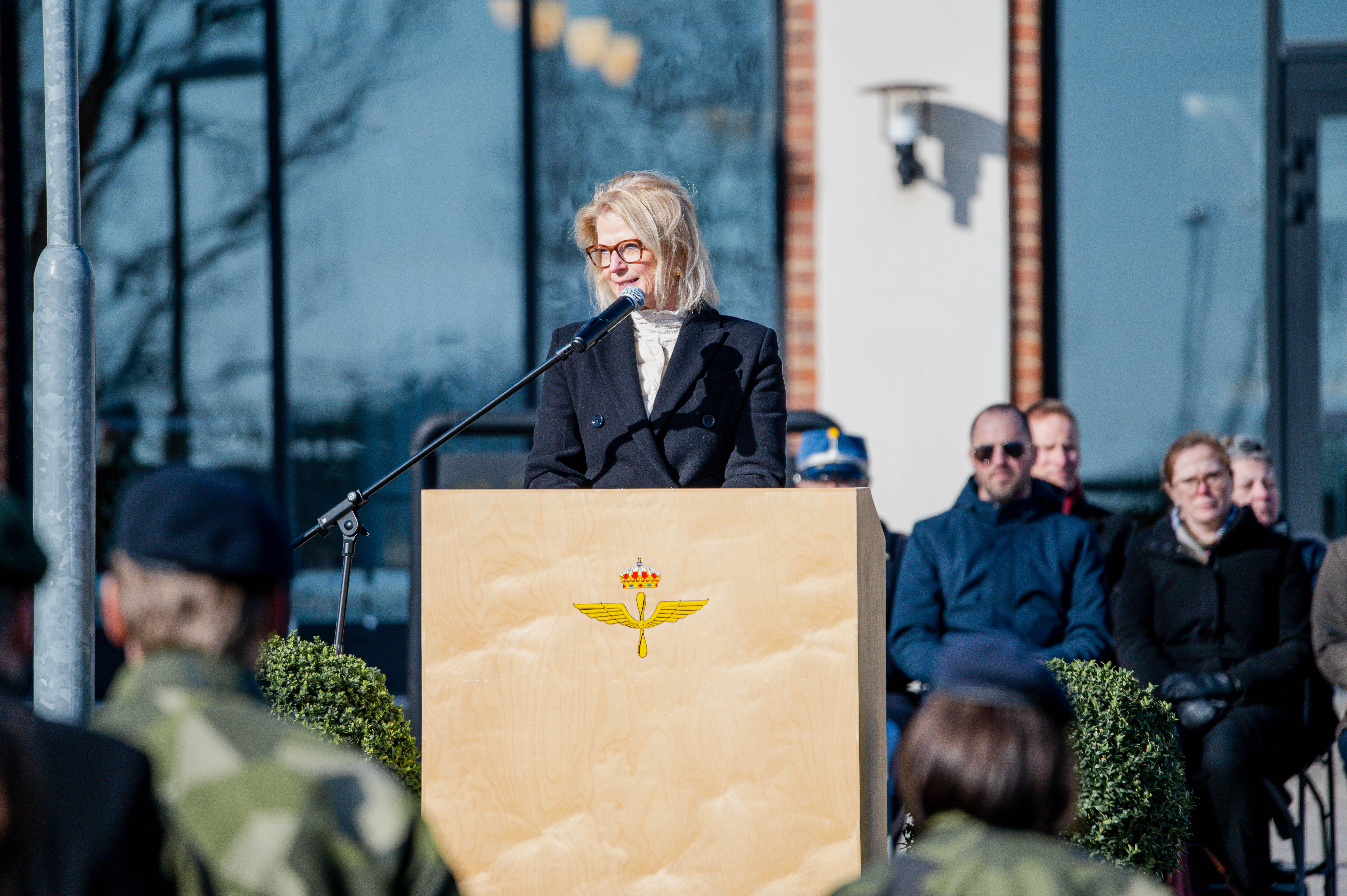 Elisabeth bakom en mikrofon utomhus med blåst i håret.