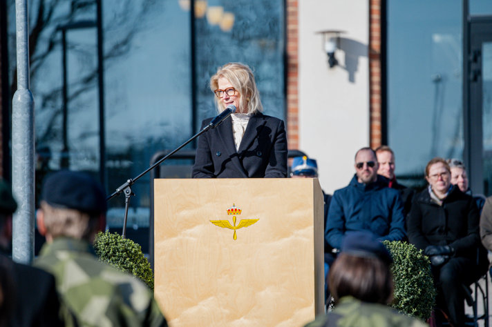 Elisabeth bakom en mikrofon utomhus med blåst i håret.