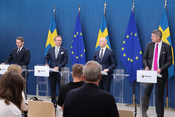 Finansmarknadsminister Niklas Wykman och  infrastruktur- och bostadsminister Andreas Carlson, Oscar Sjöstedt (SD), och Patrik Karlson (L) står på en scen framför församlade journalister.