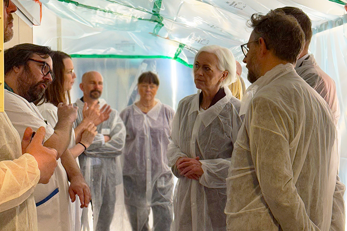 En grupp personer i vita rockar i en inplastad korridor. De samtalar med varandra,