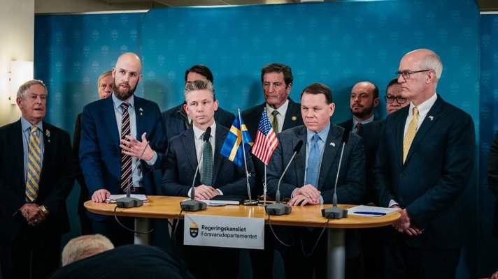 Sju ledamöter ur amerikanska kongressen står vid sidan om och bakom försvarsminister Pål Jonson och minister för civilt försvar Carl-Oskar Bohlin under en pressträff. På bordet står en svensk och en amerikansk flagga. 