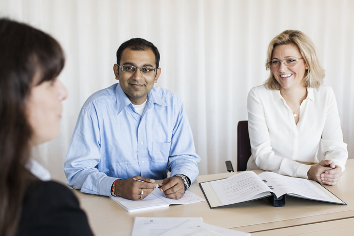En kvinna med ryggen mot betraktaren sitter i möte mittemot en man och en kvinna.