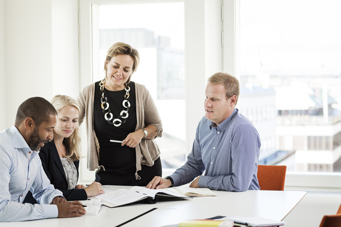 Fyra personer i möte runt ett bord. En av dem står upp.