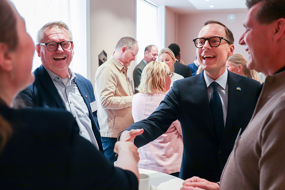 Två personer skakar hand med varandra. Ytterligare två personer står bredvid. Alla personer ser glada ut.