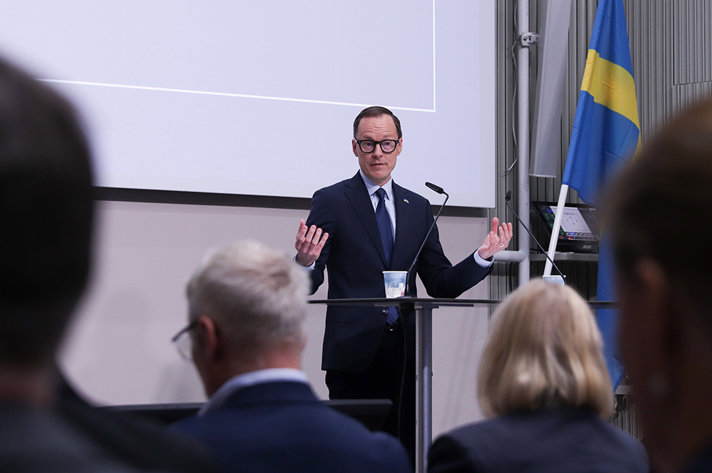 Mats Persson står på scenen och talar inför en publik. I förgrunden syns bakhuvuden på personer i publiken.