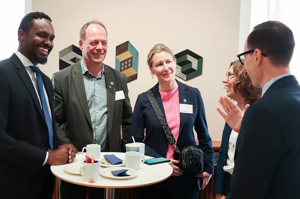 Fem personer står runt ett ståbord och samtalar. Alla ser glada ut.