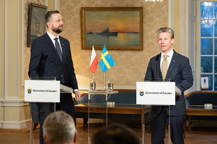 Władysław Kosiniak-Kamysz och Pål Jonson under pressträffen på Berga slott. De står vid varsitt podie på en bord mellan podierna står två bordsflaggor föreställande den polska och den svenska flaggan.