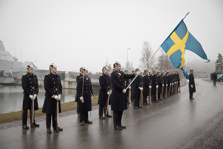 Hedersvakt står uppradade längs en kaj. En svensk flagga syns i fokus hållen en vakt.