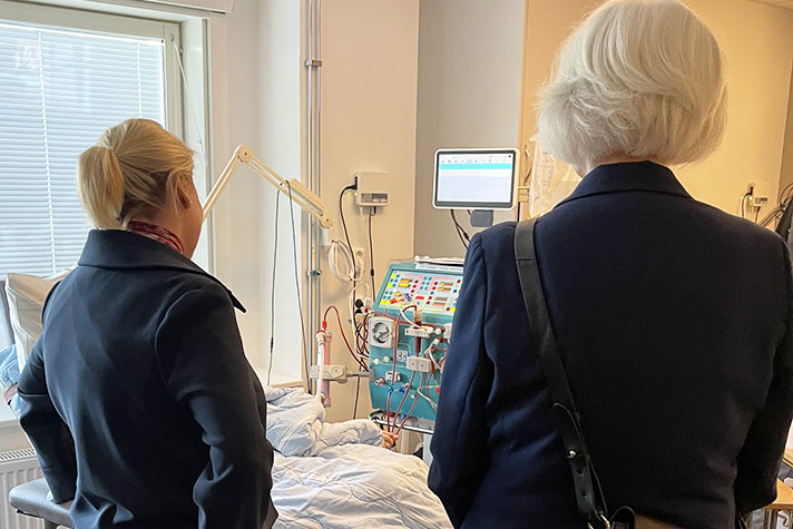 Två personer med ryggen mot kameran. I bakgrunden syns medicinsk utrustning.