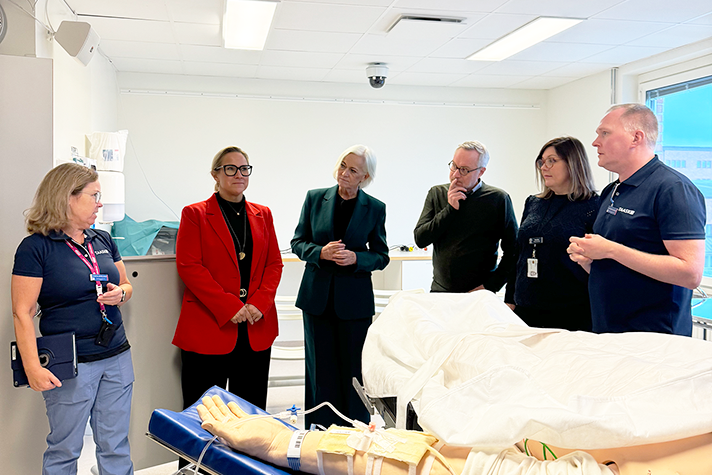 En grupp personer i en sjukhusmiljö. I förgrunden syns en armen av en träningsdocka.