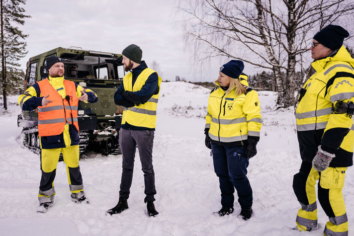 Minister för civilt försvar Carl-Oskar Bohlin står vid en bandvagn i ett snötäckt landskap med fyra medlemmar från Bilkåren.