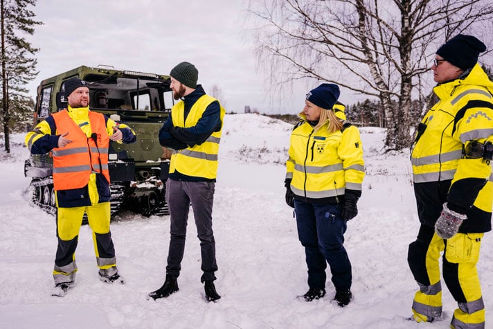 Minister för civilt försvar Carl-Oskar Bohlin står vid en bandvagn i ett snötäckt landskap med fyra medlemmar från Bilkåren. 