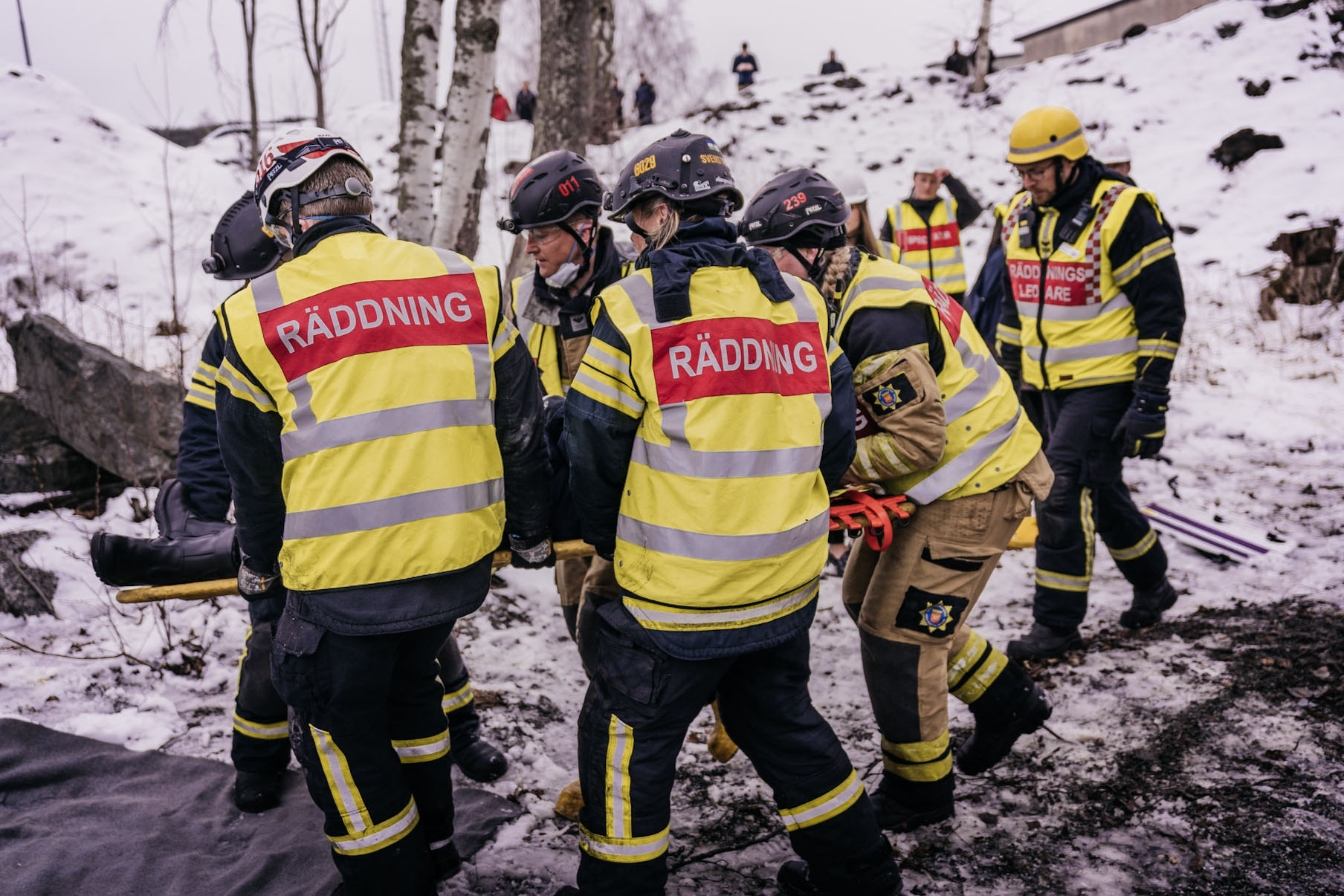 Bild på fem personer som har västar som det står "Räddning" på och som lyfter en bår.