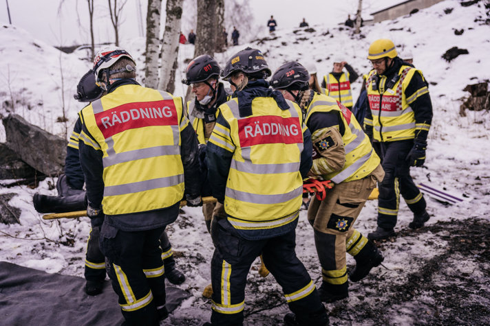 Bild på fem personer som har västar som det står "Räddning" på och som lyfter en bår.