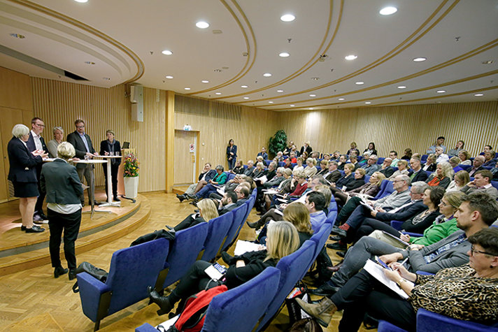Foto från sidan på en fullsatt publik som tittar mot en scen där en paneldebatt pågår.